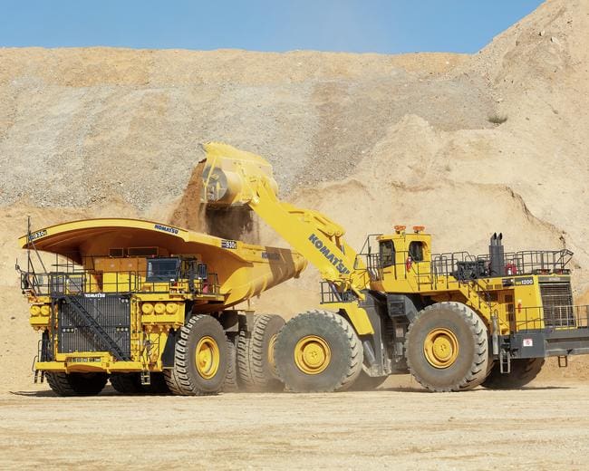 A large yellow dump truck and a smaller one in the dirt.